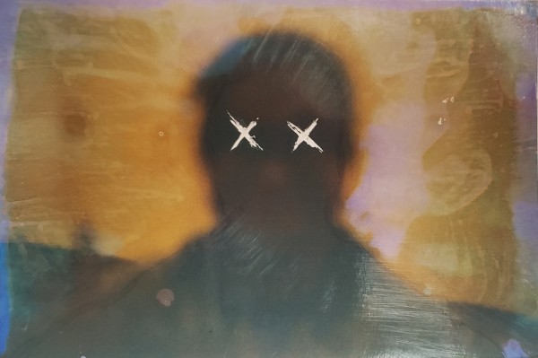 Ashley Narine, Losing Focus, 2022. Image description: A portrait consisting of a person's face and shoulders, too blurry for any features to be recognizable. Over the area of their eyes are two white Xs. The background is mottled dark yellow, with some areas of light pink.
